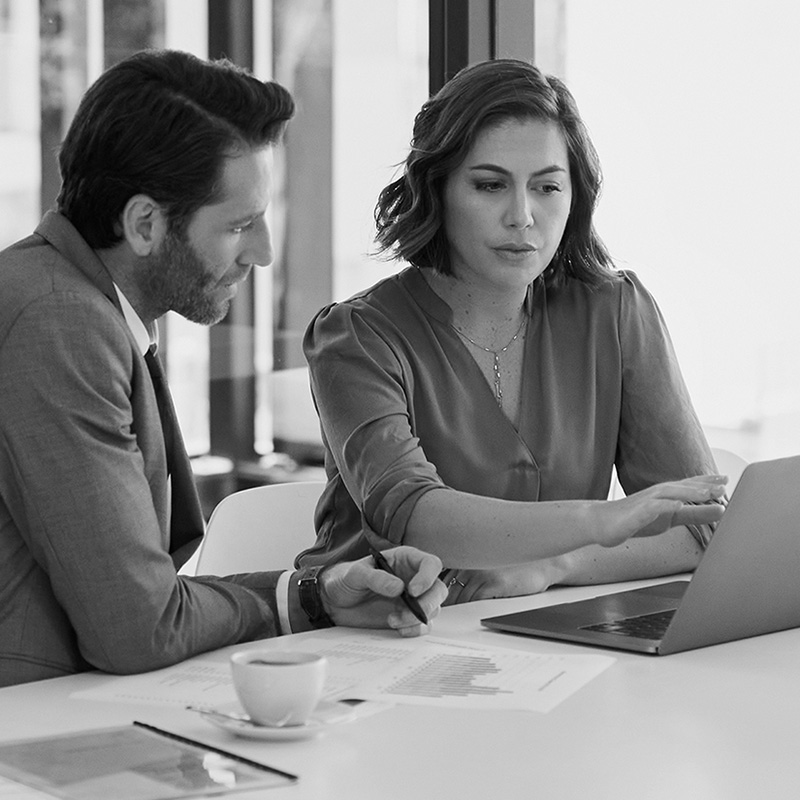 Eine Frau und ein Mann am Schreibtisch im Böro. Beide schauen konzentriert auf einen Laptop, währen die Frau mit der Hand auf den Bildschirm zeigt.